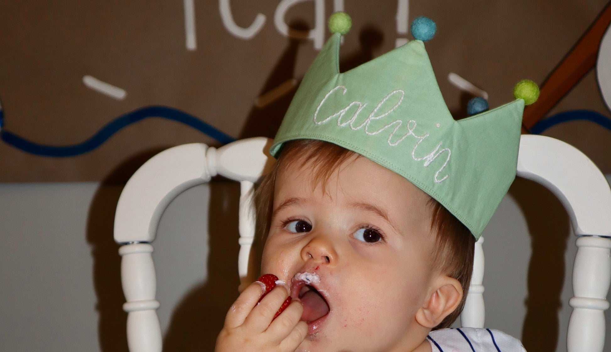 Child wearing a green birthday crown eating cake with strawberries and blueberries.